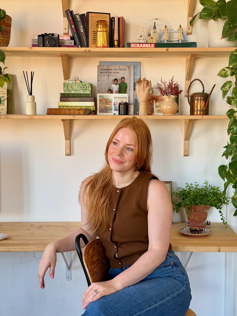 Amanda brown top, red hair, sitting at desk, plant in background
